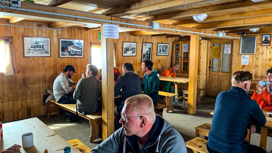 Bergsteiger sitzen im holzvertäfelten Gastraum der Capanna Margherita und nehmen ihre Mahlzeiten ein.