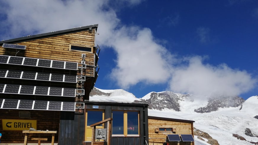 Hauptgebäude des Rifugio Quintino Sella al Felik mit mehreren Solarmodulen in hochalpiner Gletscherlandschaft.