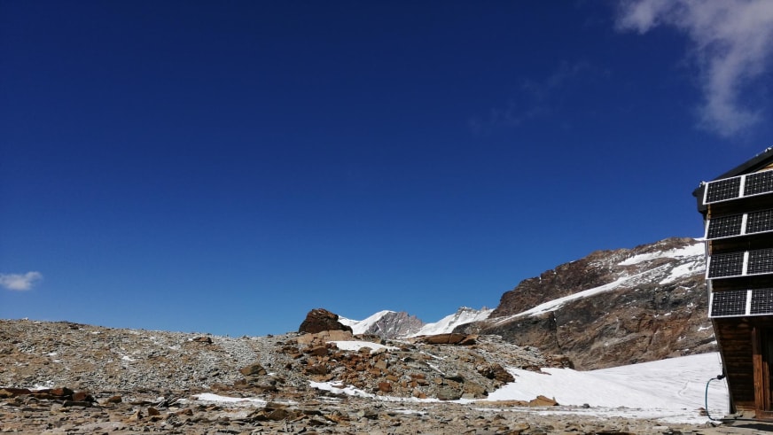 Blick auf das Rifugio Quintino Sella al Felik umgeben von Firn und Gletscherflächen in hochalpiner Umgebung.