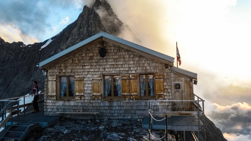 Die Mittellegihütte am Mittellegigrat mit Person auf der Terrasse bei warmem Abendlicht.