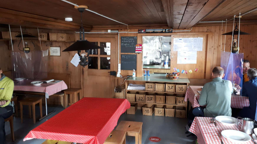 Gemütlicher Gastraum der Rothornhütte mit Holztischen, karierten Tischdecken und Bergsteigern bei der Einkehr.