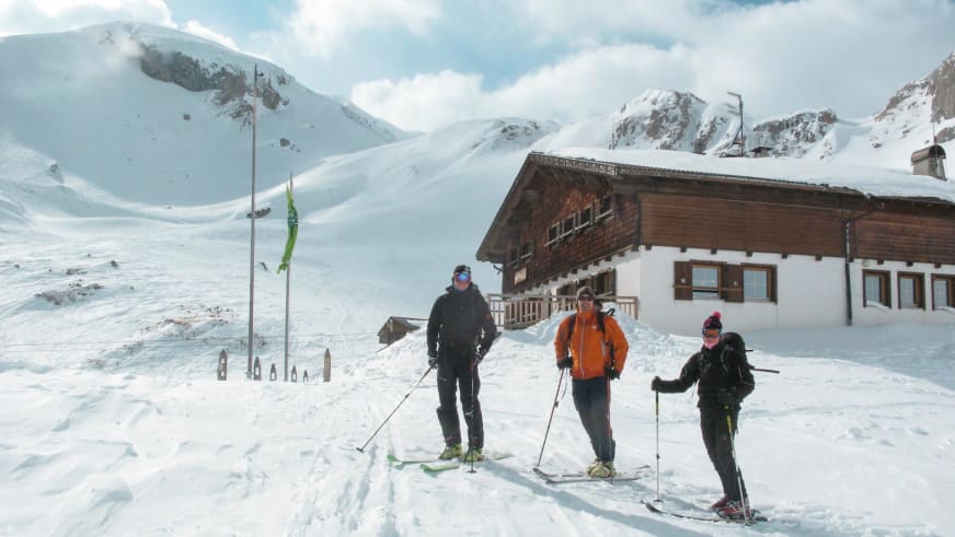 Drei Skitourengeher stehen vor der Sesvenna Hütte in verschneiter Hochgebirgslandschaft auf 2.262 m.