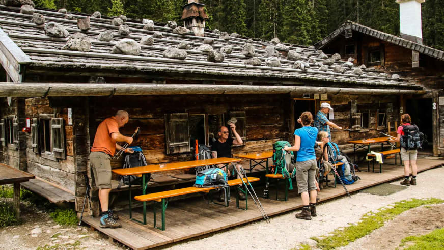 Bergwanderer machen Pause auf der Holzterrasse der Wasseralm mit traditionellem Steindach.