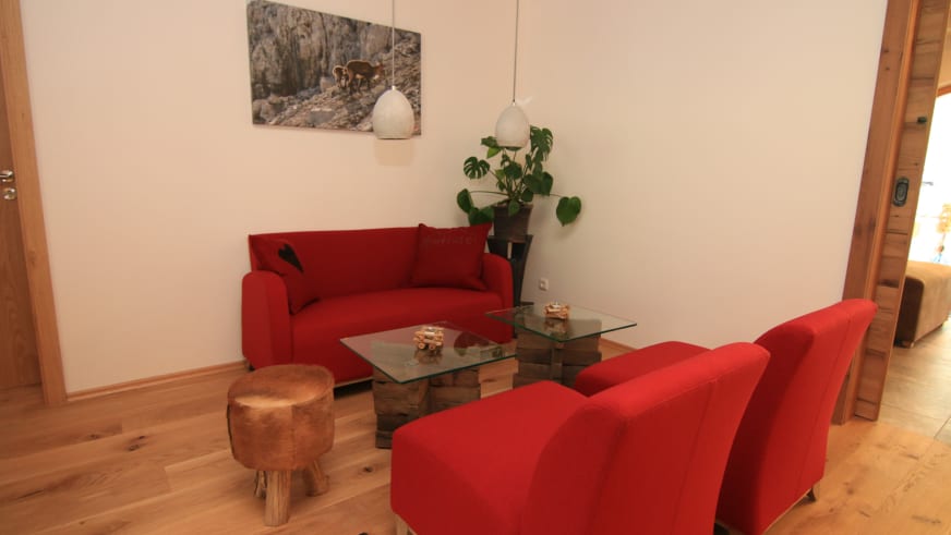 Gemütlicher Wohnbereich im Alpinhotel Berchtesgaden mit roter Polstergarnitur und Holzparkett.