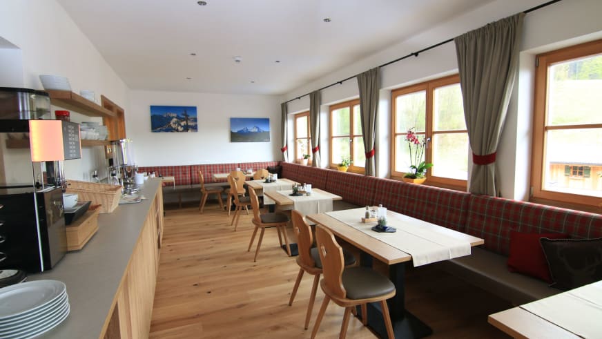 Traditioneller Gastraum im Alpinhotel Berchtesgaden mit karierter Eckbank und offener Küche.