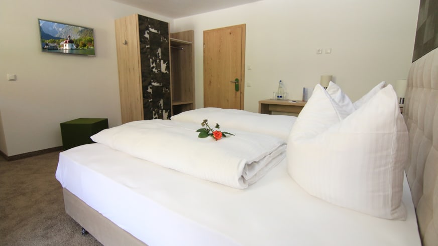 Einladend gestaltetes Zimmer im Alpinhotel Berchtesgaden mit Doppelbett und roter Rose als Dekoration.