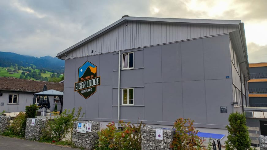 Das Hauptgebäude der Eiger Lodge zeigt eine graue Metallfassade mit großem Grindelwald-Logo an der Front.