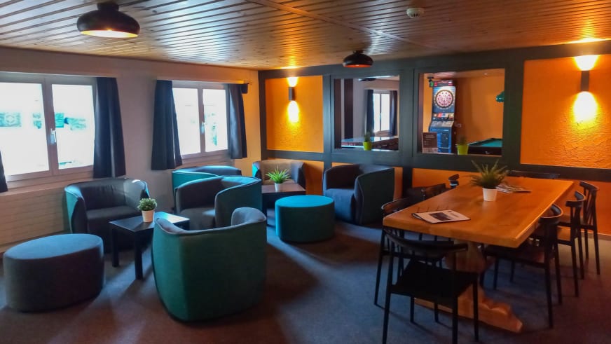 Aufenthaltsraum der Eiger Lodge mit türkisfarbenen Sesseln, Esstisch und warmem Kunstlicht.