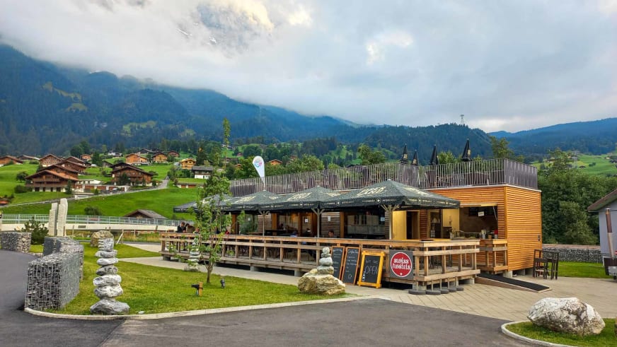 Café der Eiger Lodge als moderner Holzbau mit großen Glasfronten und umlaufender Terrasse.