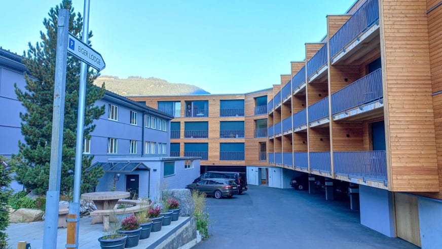 Die Eiger Lodge zeigt sich als moderner Holzbau mit drei Stockwerken und blauen Balkonen in Grindelwald.