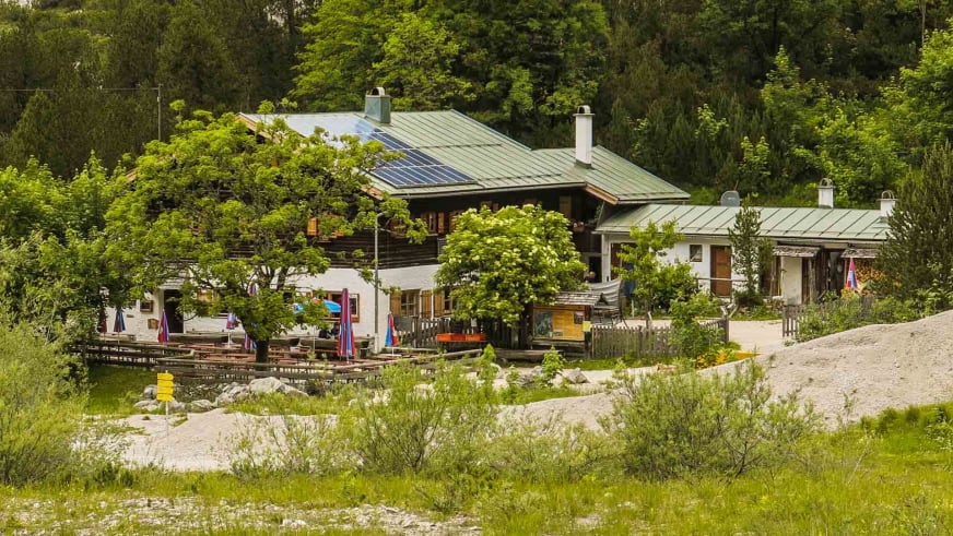 Blick auf die Wimbachgrieshütte mit grünem Blechdach und Terrasse, umgeben von dichtem Bergwald.
