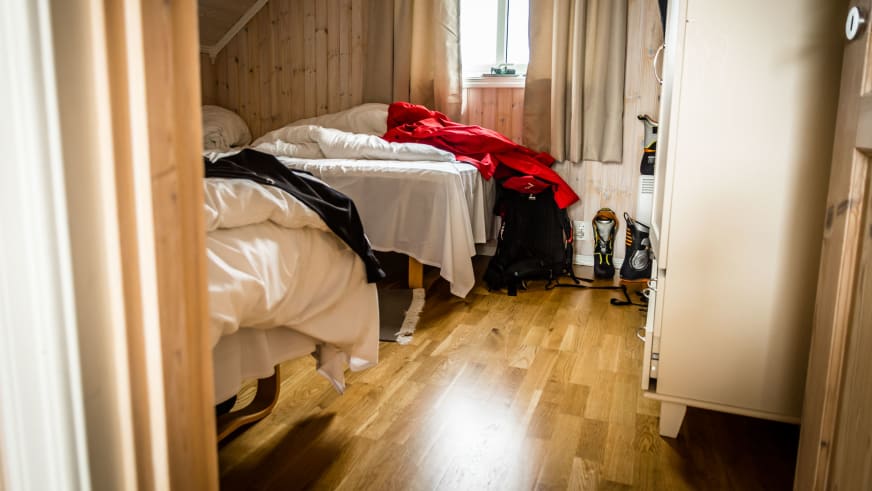 Zwei Einzelbetten im Schlafzimmer der Svinoya Rorbuer mit heller Holzverkleidung und Bergausrüstung am Boden.