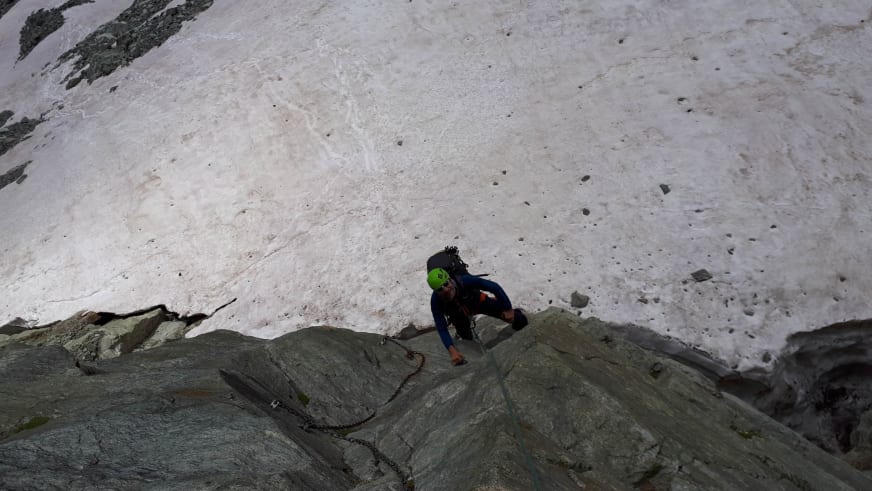 Bergsteiger klettert an grauer Granitfelswand auf dem Zustiegsweg zum Arbenbiwak über Firn und Fels.