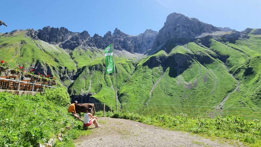 Terrasse der Kemptner Hütte mit Holztischen und Blick auf die grünen Hänge der Allgäuer Alpen.