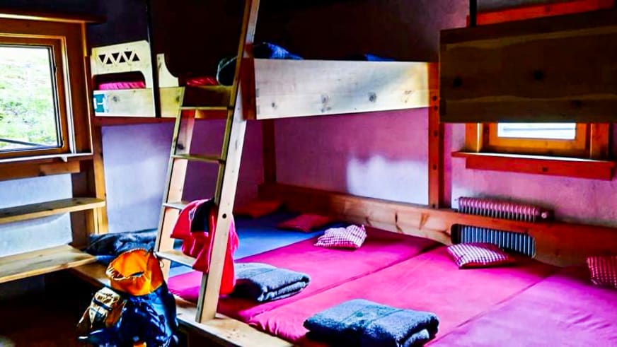 Etagenbetten aus Holz im Mehrbettzimmer der Braunschweiger Hütte mit violetten Wänden und karierten Kissen.