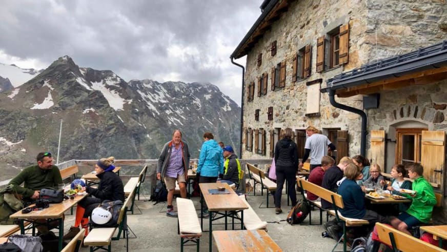 Wanderer und Familien auf der Hüttenterrasse der Braunschweiger Hütte bei der Rast vor steilen Berghängen.