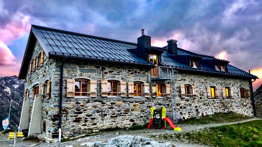Außenansicht der Braunschweiger Hütte aus Naturstein mit Kinderrutsche vor dem Eingang zur Dämmerungszeit.