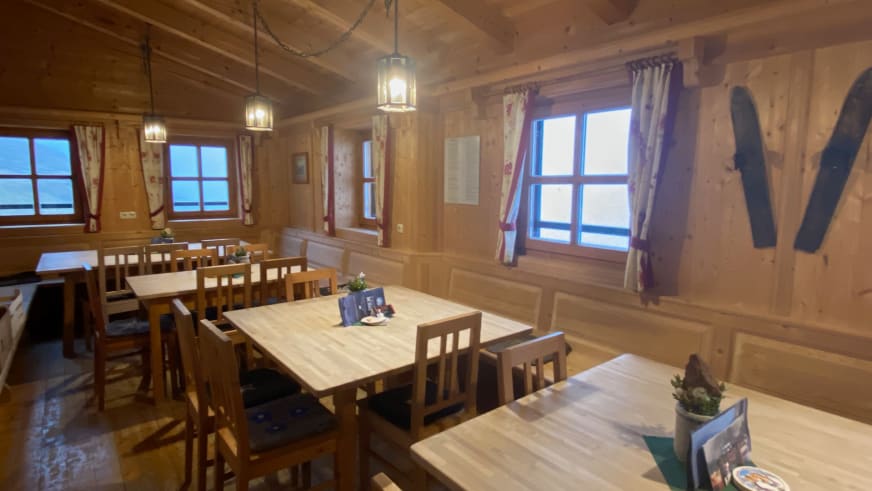 Gaststube der Warnsdorfer Hütte mit Holztischen und modernen Pendelleuchten unter Holzdecke.