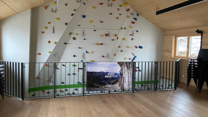 Kletterwand der Warnsdorfer Hütte im Dachgeschoss mit Pure Mountain Banner und bunten Griffen.