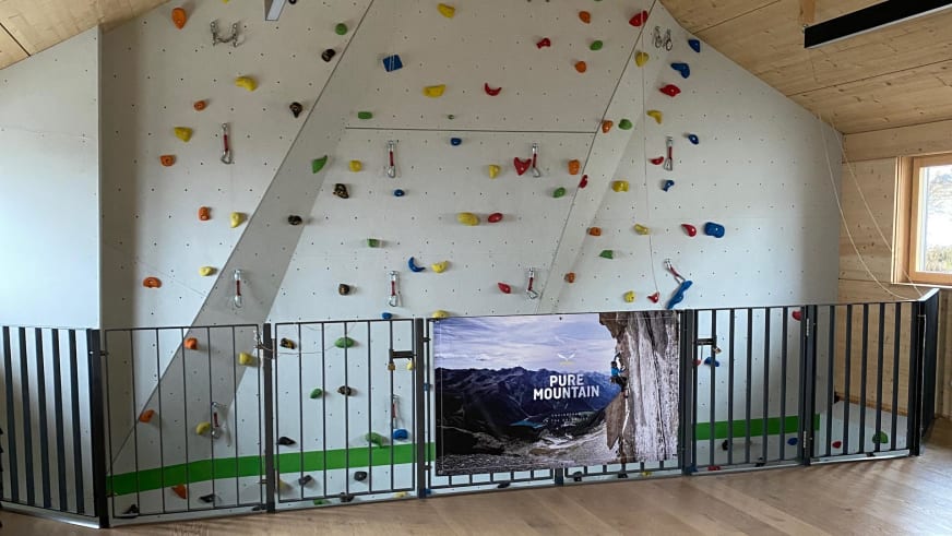 Kletterwand der Warnsdorfer Hütte unter der Dachschräge mit bunten Griffen und Metallhaken für Seilsicherung.