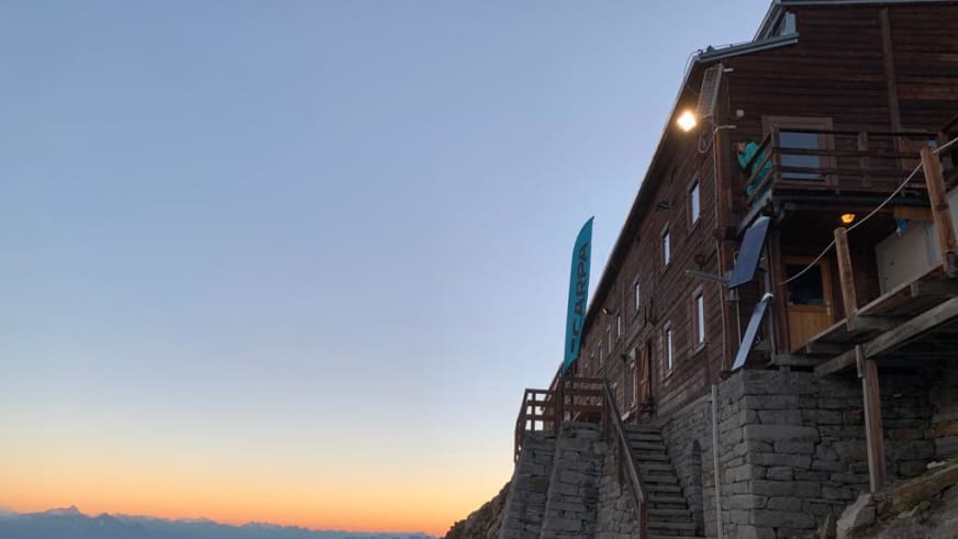 Außenansicht der Capanna Gnifetti bei Abenddämmerung mit beleuchteten Fenstern.