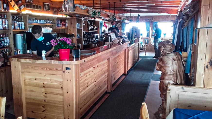 Der Gastraum des Rifugio Lagazuoi zeigt eine traditionelle Holztheke mit Mitarbeiter im Service.