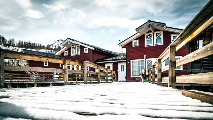 Schneebedeckter Innenhof der Koppangen Brygger Anlage mit drei roten Holzhäusern und Holzterrassen im norwegischen Stil.