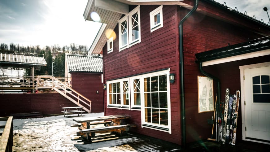 Rotes Holzgebäude der Koppangen Brygger mit weißen Fenstern und mehreren Skiern vor dem Eingang im Winter.