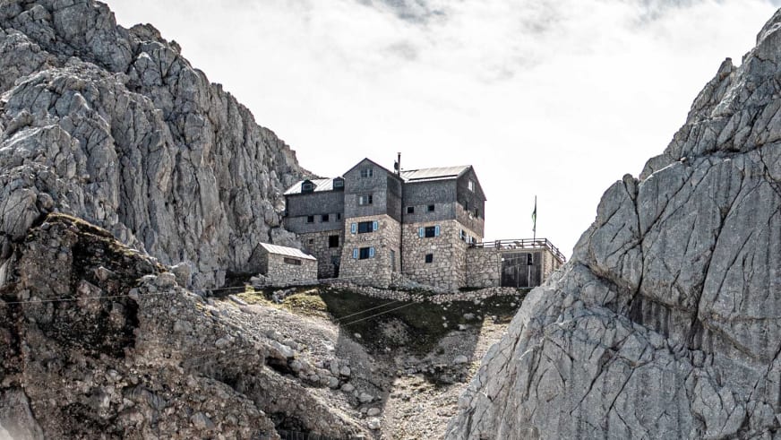 Die Meilerhütte aus hellem Naturstein steht in exponierter Lage zwischen schroffen Felswänden im Wettersteingebirge.