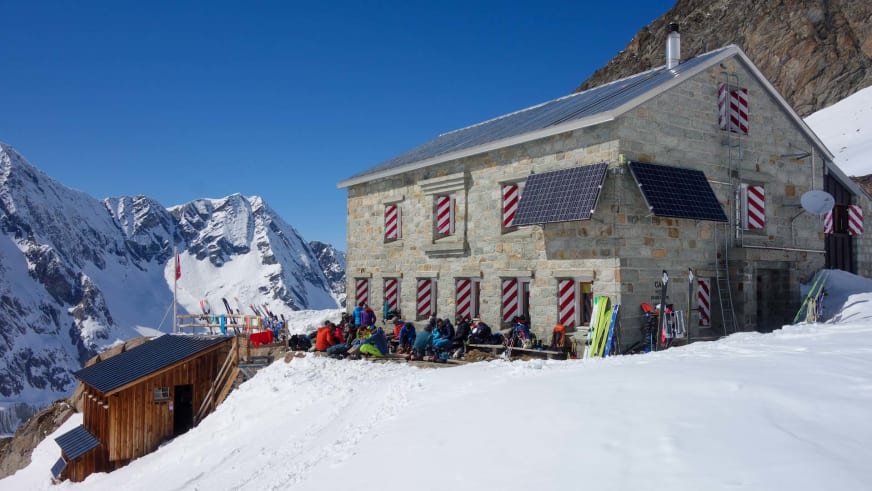 Skitourengeher pausieren vor der Cabane du Grand Mountet bei strahlendem Winterwetter.