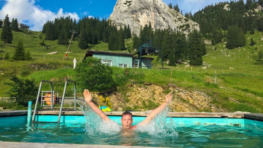 Badegast im Schwimmbecken mit Blick auf die Obere Maxlraineralm und Bergpanorama im Hintergrund.