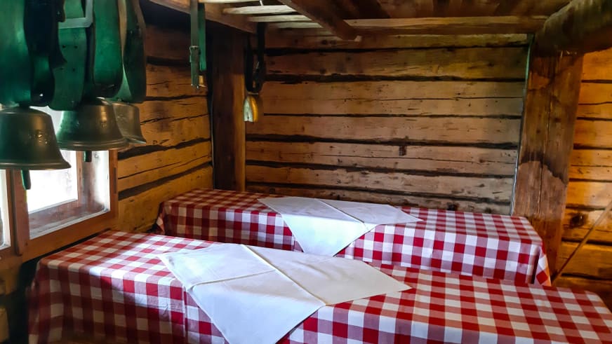 Rustikaler Gastraum in der Oberen Maxlraineralm mit Holzbänken und rot-weiß karierten Tischdecken.