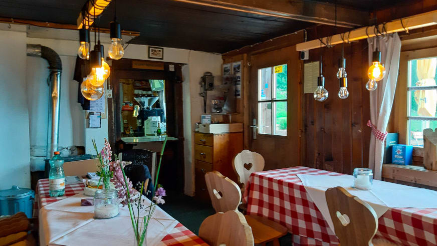 Gaststube der Oberen Maxlraineralm mit gedeckten Tischen und herzförmigen Holzstühlen unter Edison-Beleuchtung.
