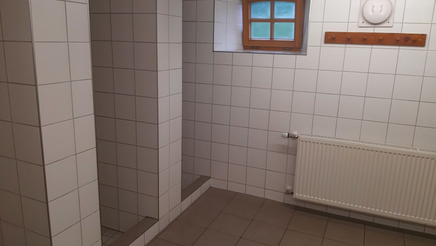 Gefliester Duschbereich in der Albert-Link-Hütte mit offener Dusche und Heizung unter kleinem Fenster.