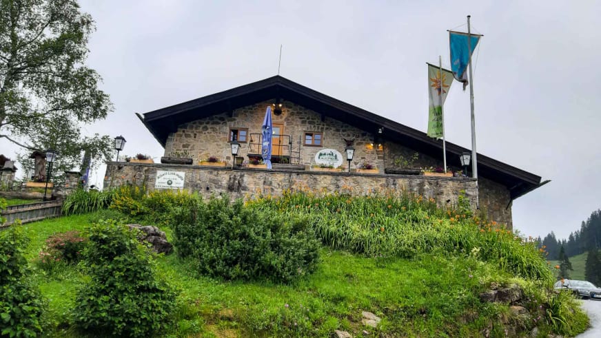 Außenansicht der Albert-Link-Hütte mit Natursteinfassade und Satteldach inmitten grüner Vegetation.