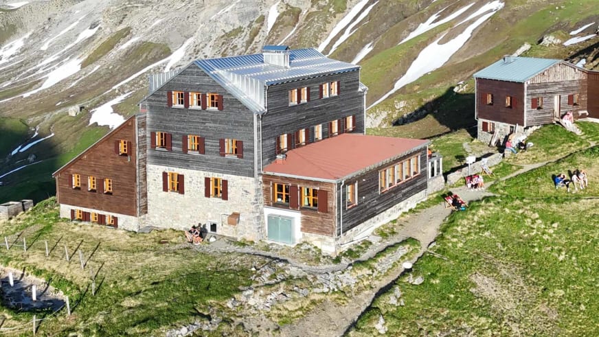 Luftaufnahme der Stuttgarter Hütte mit mehreren Gebäuden und Wanderern auf der Terrasse in hochalpiner Lage.
