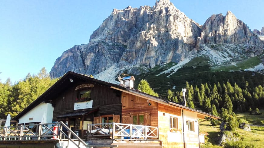 Das Rifugio Col Gallina mit großer Terrasse und weißen Sonnenschirmen vor hohen Kalksteinwänden.