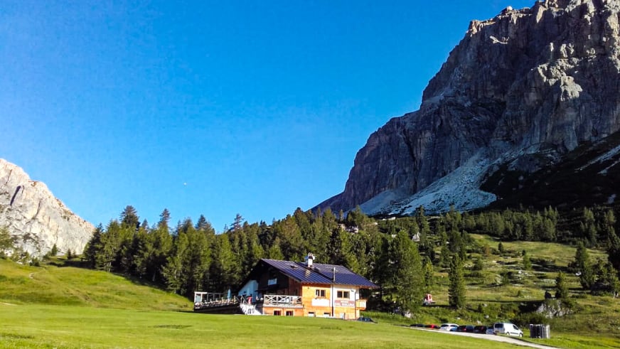 Panoramablick auf das Rifugio Col Gallina inmitten grüner Almwiesen vor hohen Dolomiten-Felswänden.