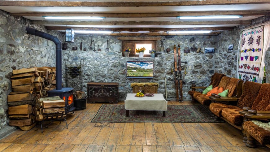 Traditionelle Lounge der Villa Mestia mit Natursteinwänden, brennendem Kamin und alter Skiausrüstung an den Wänden.