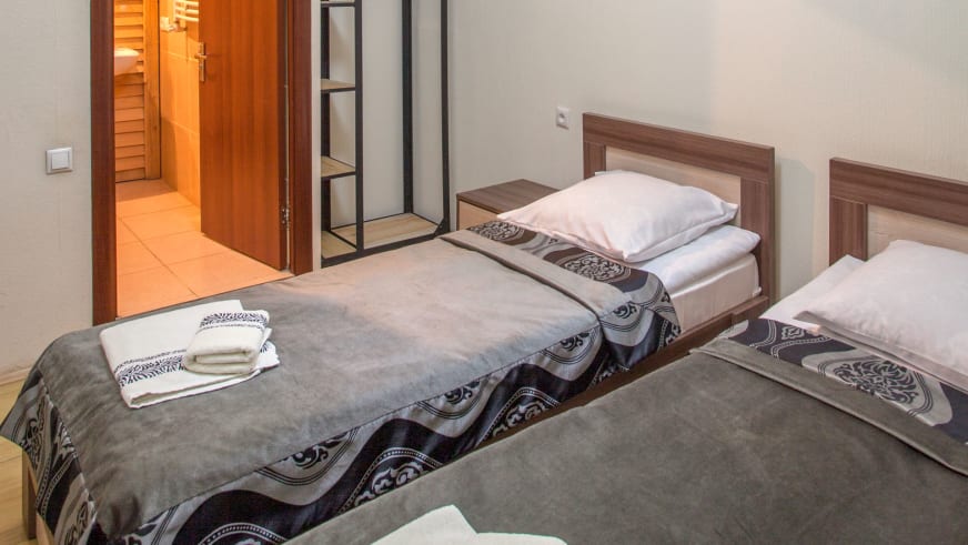 Doppelzimmer der Villa Mestia mit zwei Einzelbetten, dunklen Holzkopfteilen und grauem Teppichboden.