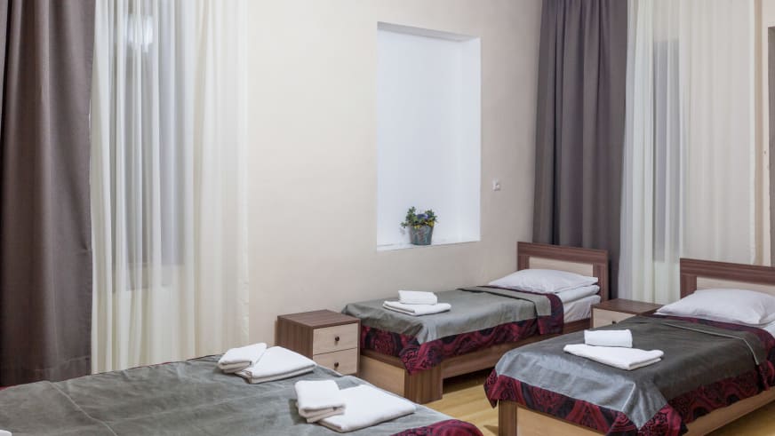 Helles Mehrbettzimmer der Villa Mestia mit drei Einzelbetten aus Holz und großen Fenstern.