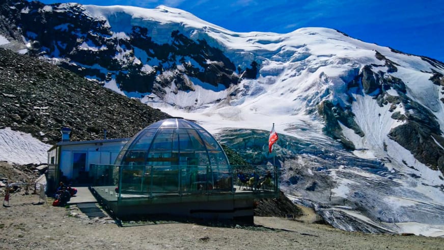 Die Hohsaashütte mit ihrer charakteristischen Glaskuppel steht vor einem schneebedeckten Gletscher im Hochgebirge.