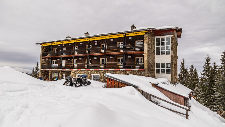 Dreistöckiges Hauptgebäude der Cabana Negoiu mit gelbem Balkon und dicke Schneeschicht auf dem Dach.