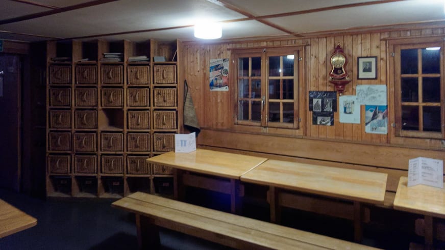 Gastraum der Cabane de Bertol mit traditionellen Holzfächern, Holztischen und Sprossenfenstern in der Wand.