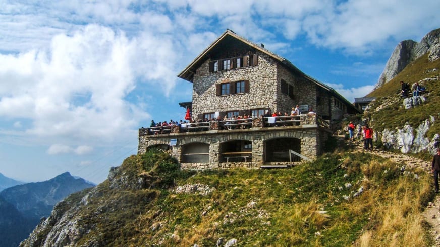 Wanderer versammeln sich auf der Terrasse der Bad Kissinger Hütte am steilen Berghang mit Blick ins Tal.