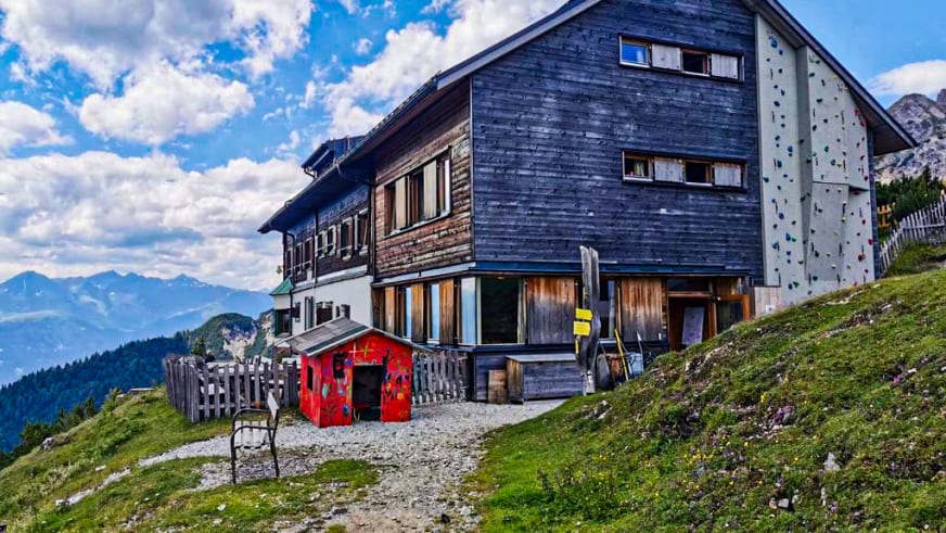 Das Solsteinhaus zeigt sich als traditionelle Holzhütte mit modernem Anbau auf einer Almwiese im Karwendel.