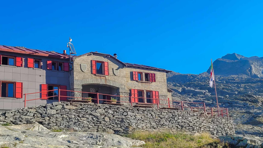 Das Rifugio Ponti zeigt eine Mischung aus modernem Anbau und traditionellem Steinbau mit roten Fensterläden.
