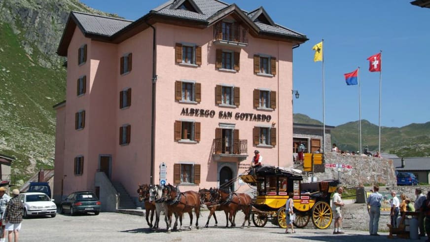 Das rosa Albergo San Gottardo am Gotthardpass mit einer historischen Postkutsche vor dem Haupteingang.