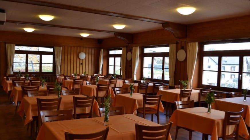 Gastraum im Albergo San Gottardo mit traditioneller Holzvertäfelung und orangefarbenen Tischdecken.