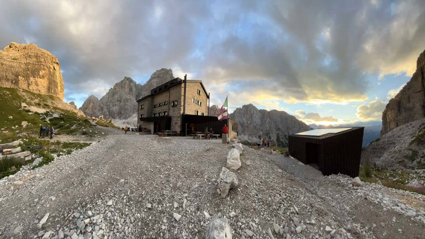 Bergwanderer vor dem Rifugio Brentei auf einem Schuttplateau in den Dolomiten bei bewölktem Himmel.